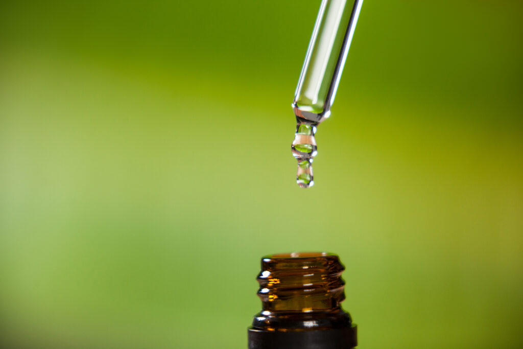 Nahaufnahme eines Öltropfens, der aus einer Pipette in eine Flasche mit ätherischem Öl tropft