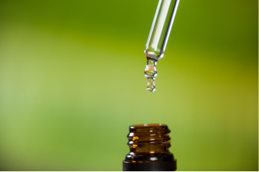Nahaufnahme eines Öltropfens, der aus einer Pipette in eine Flasche mit ätherischem Öl tropft um ein Heilmittel für Homöopathie darzustellen